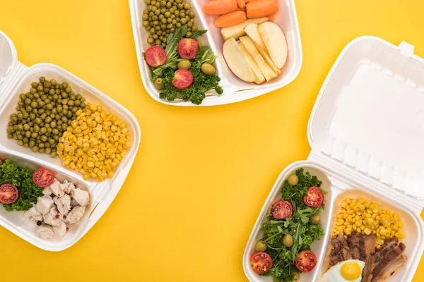 Vista dall'alto di confezioni ecologiche con mele, verdure, carne, uova fritte e insalate isolate sul giallo — Foto stock