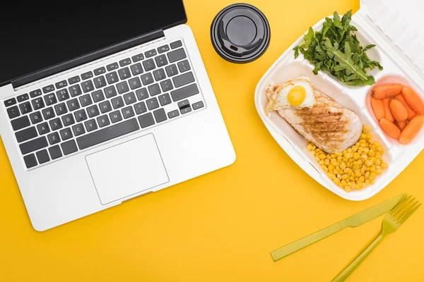 Vista superior de copo de papel, laptop e pacote ecológico com legumes, carne, ovo frito e rúcula isolada em amarelo — Fotografia de Stock