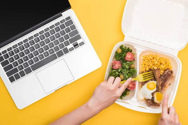 Vista ritagliata della donna che mangia dal pacchetto eco con mais, carne, uova fritte e insalata isolata sul giallo — Foto stock