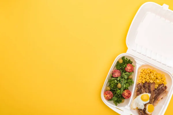 Top view of eco package with corn, meat, fried eggs and salad isolated on yellow — Stock Photo