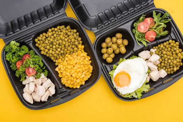 Vista superior de los paquetes ecológicos con verduras, carne, huevo frito y ensaladas aisladas en amarillo - foto de stock
