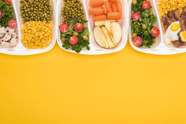 Вид зверху на екологічні пакети з яблуками, овочами, м'ясом, смаженими яйцями та салатами ізольовані на жовтому — стокове фото