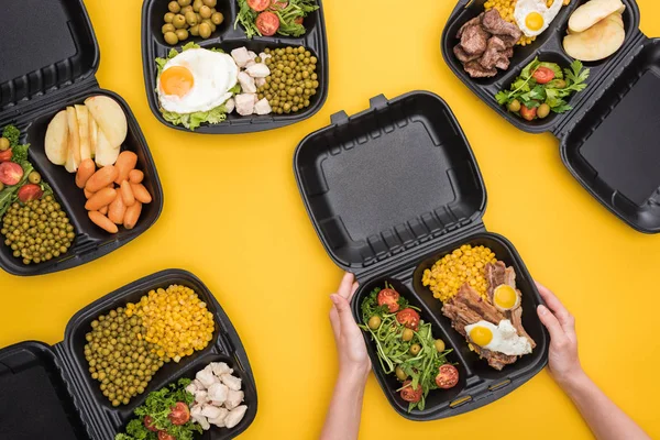 Vista recortada de la mujer sosteniendo eco paquete con maíz, carne, huevos fritos y ensalada aislada en amarillo - foto de stock