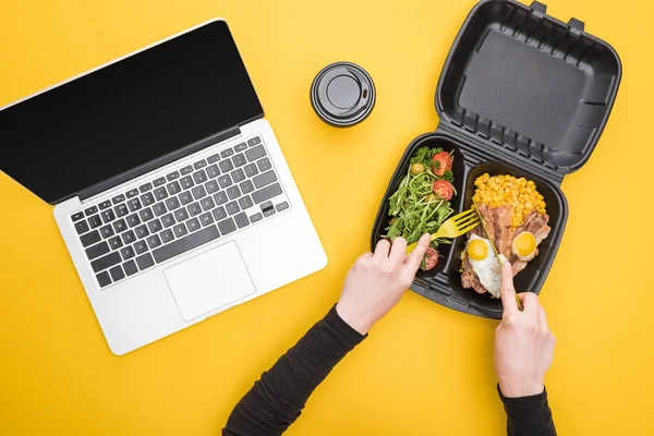 Vista ritagliata della donna che mangia dal pacchetto eco con mais, carne, uova fritte e insalata isolata sul giallo — Foto stock