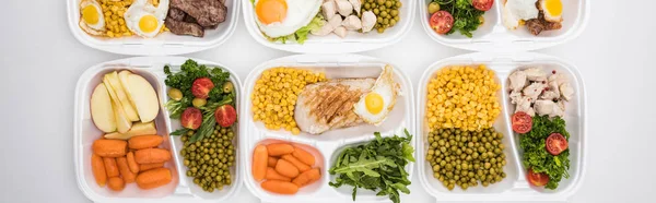 Plano panorámico de paquetes ecológicos con manzanas, verduras, carne, huevos fritos y ensaladas sobre fondo blanco - foto de stock