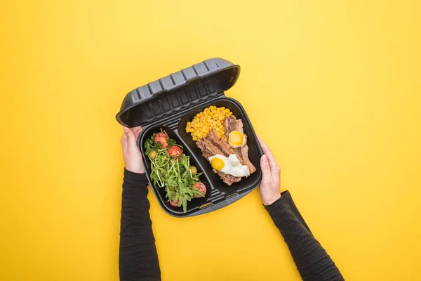 Abgeschnittene Ansicht einer Frau, die Ökopackung mit Mais, Fleisch, Spiegeleiern und Salat hält, isoliert auf gelb — Stockfoto