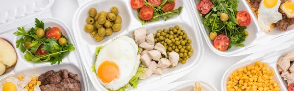 Plano panorámico de paquetes ecológicos con manzanas, verduras, carne, huevos fritos y ensaladas sobre fondo blanco - foto de stock