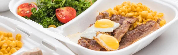 Panoramic shot of eco package with corn, meat, fried eggs and salad on white background — Stock Photo