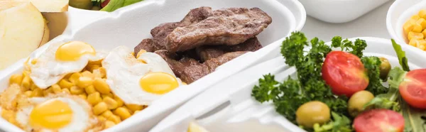 Panoramic shot of eco package with corn, meat, fried eggs and salad on white background — Stock Photo