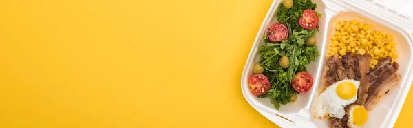 Panoramic shot of eco package with corn, meat, fried eggs and salad isolated on yellow — Stock Photo