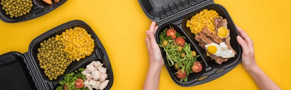 Plano panorámico de mujer sosteniendo eco paquete con maíz, carne, huevos fritos y ensalada aislada en amarillo - foto de stock