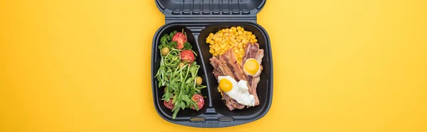 Panoramic shot of eco package with corn, meat, fried eggs and salad isolated on yellow — Stock Photo