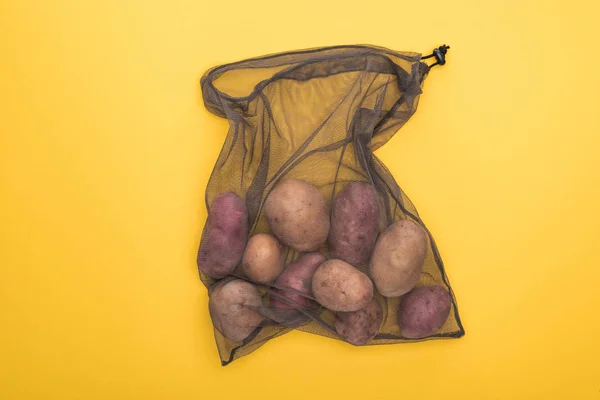 Vista superior de las patatas en bolsa de malla negra ecológica aislada en amarillo - foto de stock