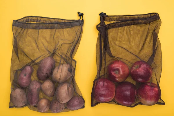 Vue du dessus des pommes de terre et des pommes dans des sacs en filet noir respectueux de l'environnement isolés sur jaune — Photo de stock
