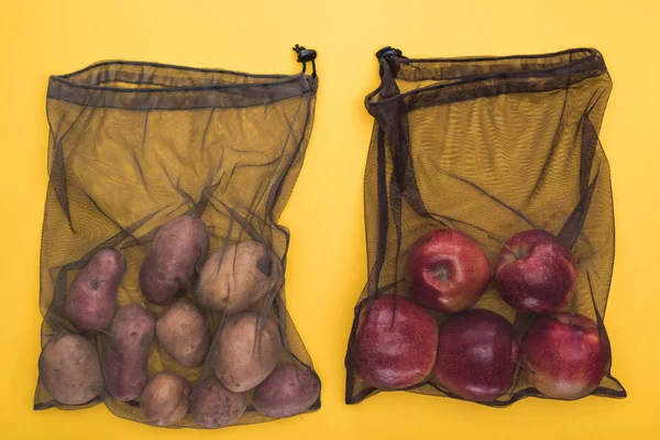 Vista superior de batatas e maçãs em eco friendly sacos de malha preta isolados em amarelo — Fotografia de Stock