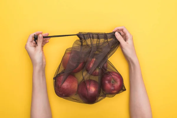 Vista recortada de la mujer sosteniendo bolsa ecológica con manzanas maduras aisladas en amarillo - foto de stock