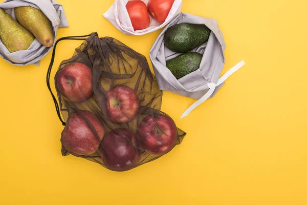 Top view of ripe apples, pears, tomatoes, avocado in eco friendly bags isolated on yellow — Stock Photo