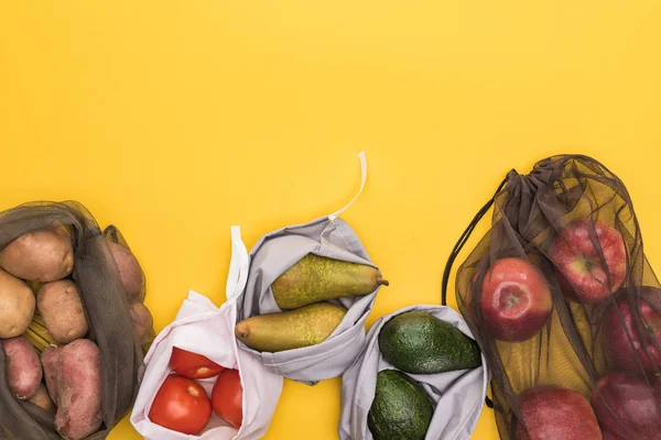 Vue de dessus des pommes mûres, poires, tomates, avocats et pommes de terre dans des sacs écologiques isolés sur jaune — Photo de stock