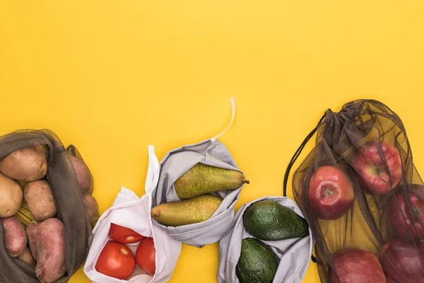 Top view of ripe apples, pears, tomatoes, avocado and potatoes in eco friendly bags isolated on yellow — Stock Photo