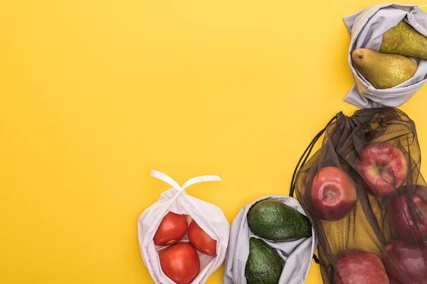 Vista superior de manzanas maduras, peras, tomates, aguacate en bolsas ecológicas aisladas en amarillo - foto de stock