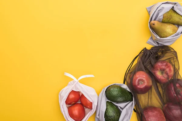 Vista superior de maçãs maduras, pêras, tomates, abacate em sacos eco friendly isolados em amarelo — Fotografia de Stock