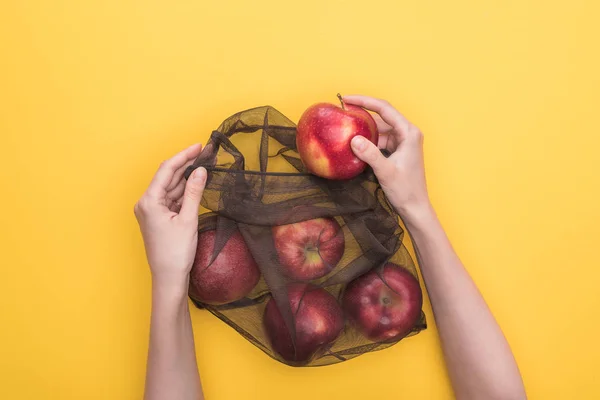 Vista parcial de la mujer sosteniendo bolsa ecológica con manzanas maduras aisladas en amarillo - foto de stock