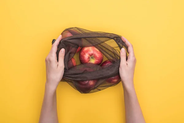 Vista parcial de la mujer sosteniendo bolsa ecológica con manzanas maduras aisladas en amarillo - foto de stock