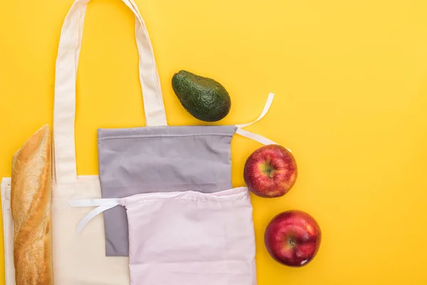 Vue de dessus des pommes mûres, de la baguette et de l'avocat près des sacs écologiques isolés sur jaune — Photo de stock