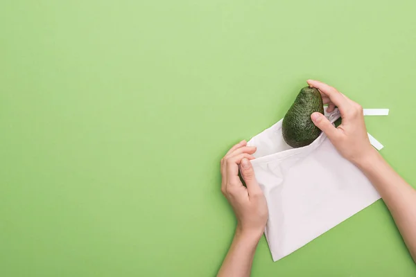 Vista recortada de la mujer poniendo aguacate en bolsa ecológica aislado en verde - foto de stock