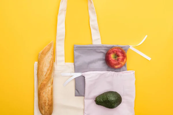 Top view of apple, baguette and avocado on eco friendly bags isolated on yellow — Stock Photo