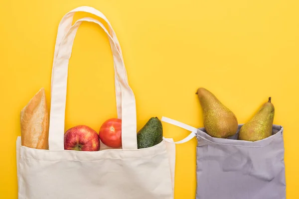 Вид зверху на стиглі фрукти, овочі та багет в екологічно чистих сумках ізольовані на жовтому — стокове фото