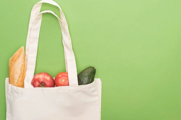 Top view of tomato, avocado, apple and baguette in eco friendly bag isolated on green — Stock Photo