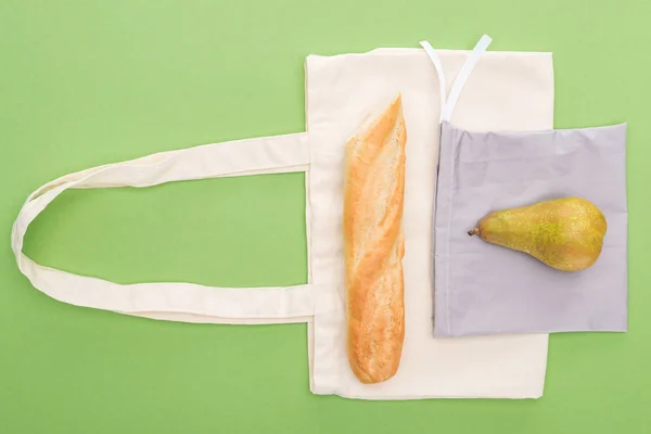 Vista superior de pera y baguette en bolsas ecológicas aisladas en verde - foto de stock