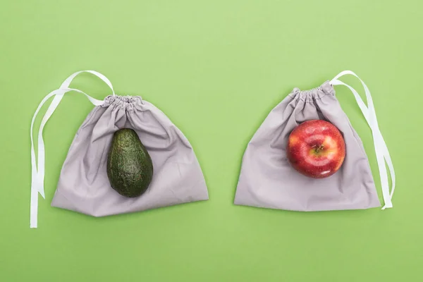 Top view of avocado and apple on eco friendly bags isolated on green — Stock Photo