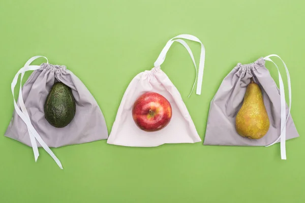 Top view of avocado, pear and apple on eco friendly bags isolated on green — Stock Photo