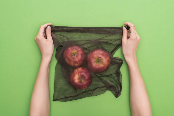 Vista parcial de la mujer sosteniendo manzanas rojas maduras en bolsa ecológica aislada en verde - foto de stock