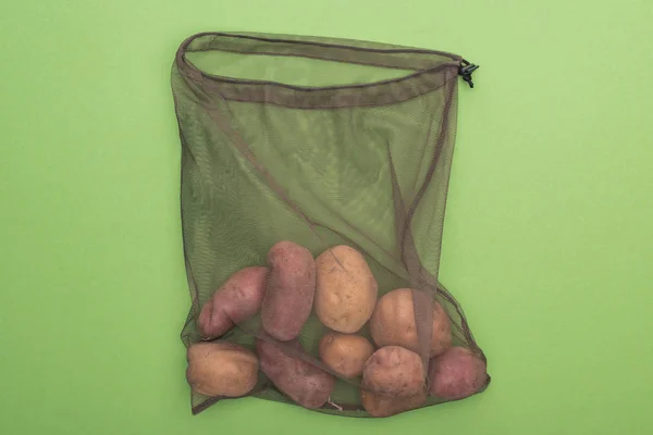 Top view of fresh whole potatoes in eco friendly bag isolated on green — Stock Photo