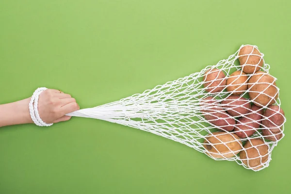 Cropped view of woman holding string bag with potatoes isolated on green — Stock Photo