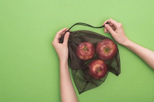 Vista parcial de la mujer sosteniendo manzanas rojas maduras en bolsa ecológica aislada en verde - foto de stock