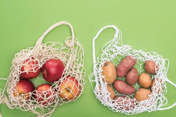 Top view of ripe apples and potatoes in string bags isolated on green — Stock Photo