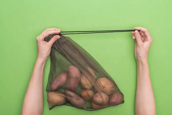 Обрізаний вид жінки, що тримає екологічно чисту сумку з картоплею ізольовано на зеленому — стокове фото
