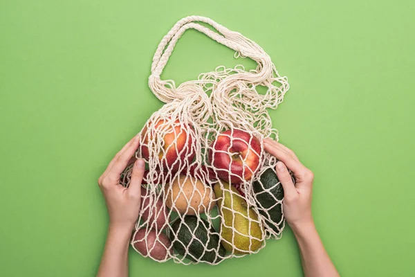 Vista superior da mulher segurando legumes e frutas no saco de cordas isolado no verde — Fotografia de Stock