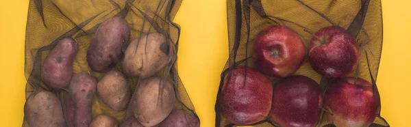 Vue du dessus des pommes de terre et des pommes dans des sacs en filet noir écologiques isolés sur une photo panoramique jaune — Photo de stock