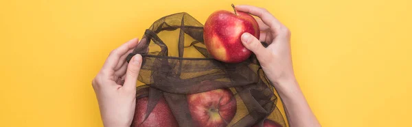 Cropped view of woman holding eco friendly bag with ripe apples isolated on yellow, panoramic shot — Stock Photo