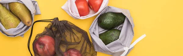 Top view of ripe apples, pears, tomatoes, avocado in eco friendly bags isolated on yellow, panoramic shot — Stock Photo