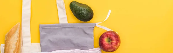 Vista superior de la manzana madura, baguette y aguacate cerca de bolsas ecológicas aisladas en amarillo, plano panorámico - foto de stock