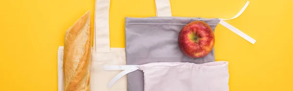 Vista superior de la manzana madura, baguette en bolsas ecológicas aisladas en amarillo, plano panorámico - foto de stock