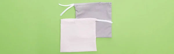 Вид зверху на екологічно чисті сірі та білі сумки ізольовані на зеленому, панорамному знімку — стокове фото