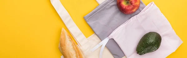 Top view of apple, baguette and avocado on eco friendly bags isolated on yellow, panoramic shot — Stock Photo