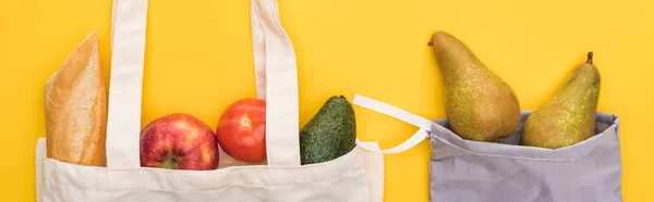 Vista superior de frutas maduras, verduras y baguette en bolsas ecológicas aisladas en amarillo, plano panorámico - foto de stock